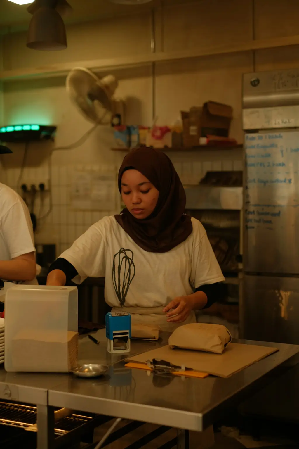 A baker in a headscarf preparing dough at a bakery counter